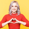 Smiling woman in a red sweater forming a heart with her hands